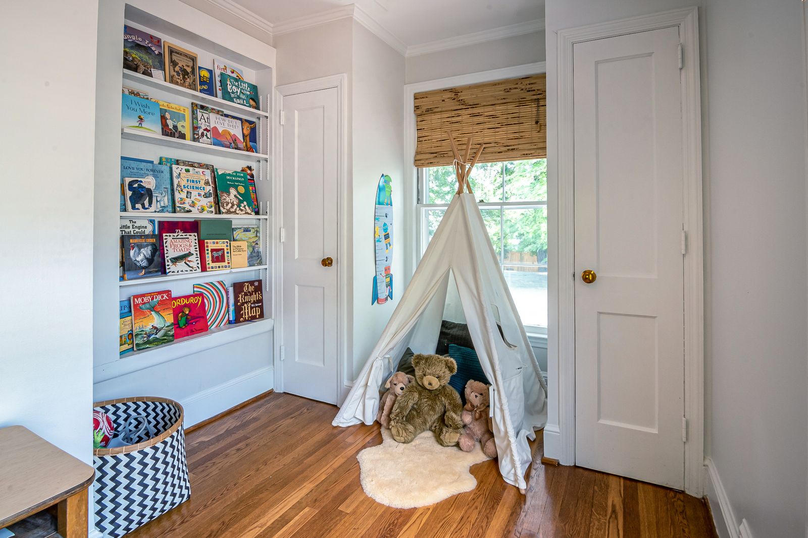 A compact, tidy corner of a shared bedroom set up for play with wall storage and a soft floor mat